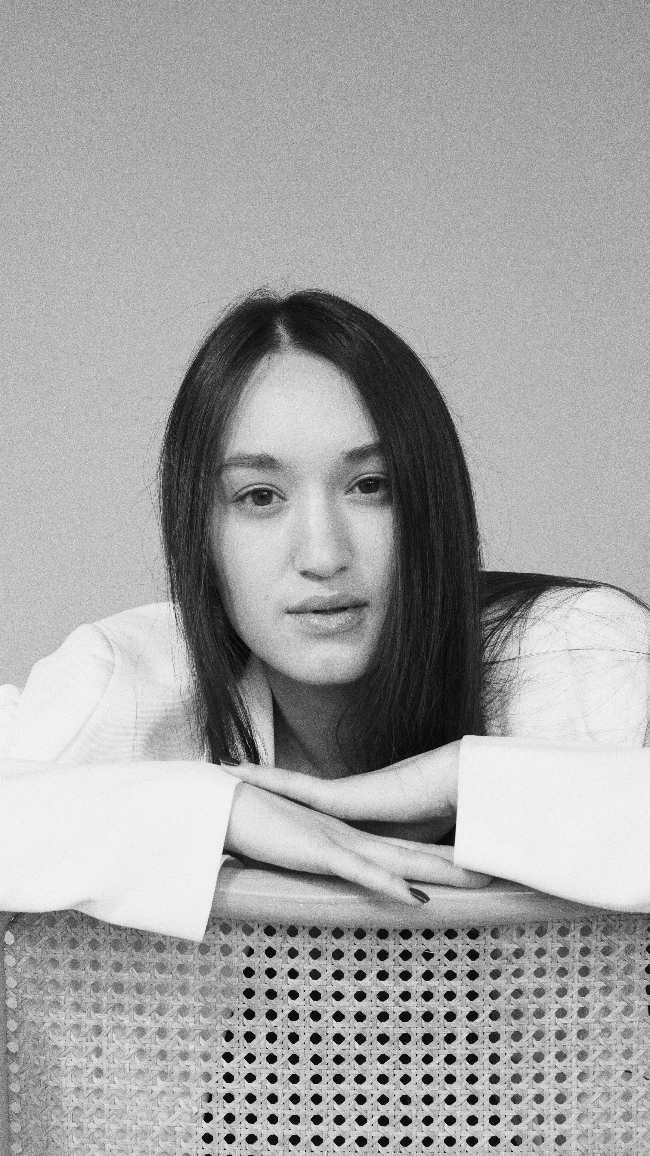 Monochrome portrait of a young woman in a white blazer posing thoughtfully indoors.