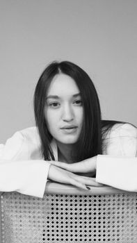 Monochrome portrait of a young woman in a white blazer posing thoughtfully indoors.