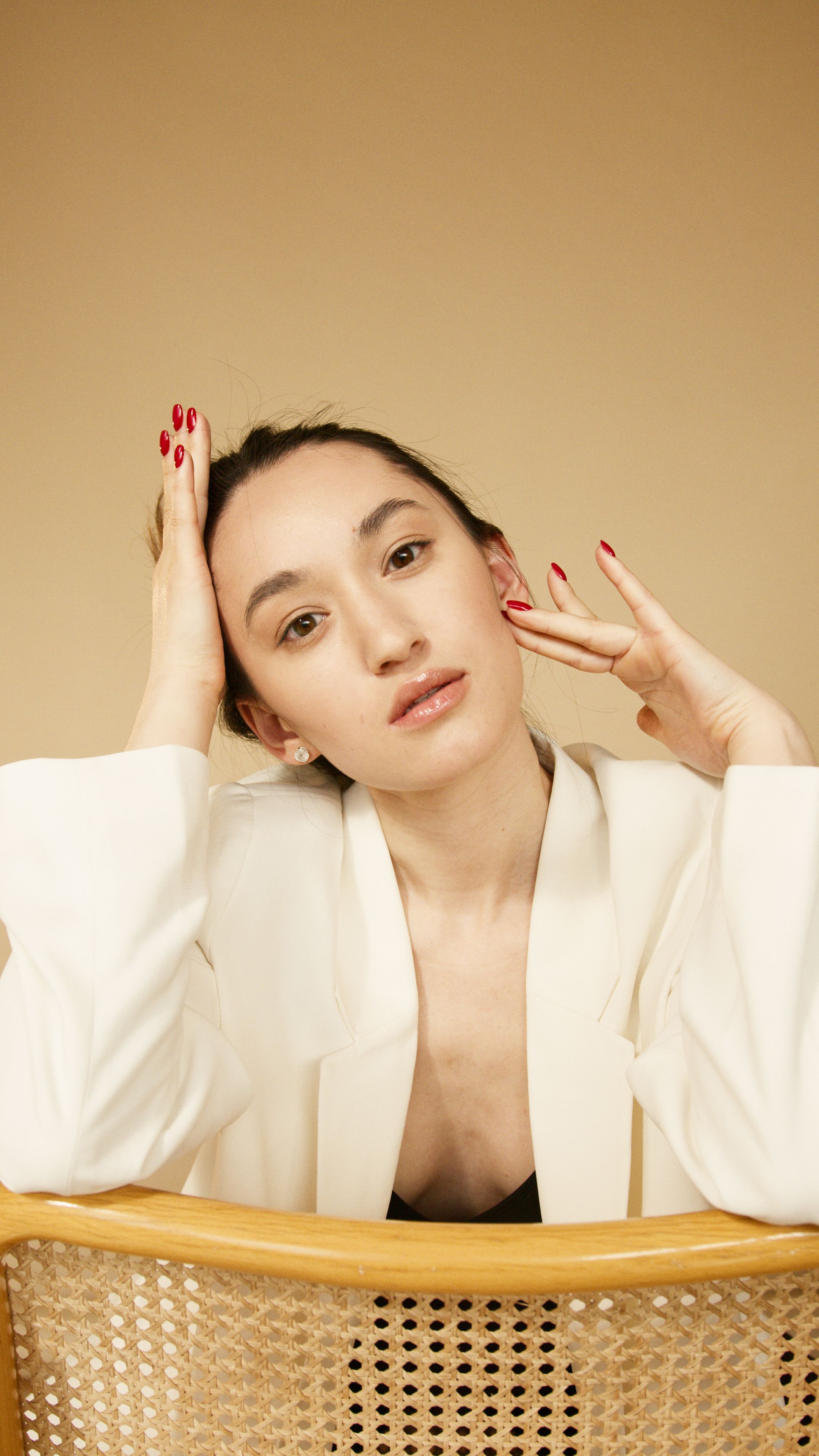 Stylish and elegant portrait of a woman in a white blazer posing thoughtfully against a beige background.