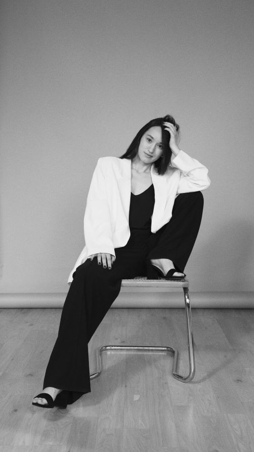 Free Black-and-white portrait of a stylish woman in a white blazer posing while sitting on a chair. Stock Photo