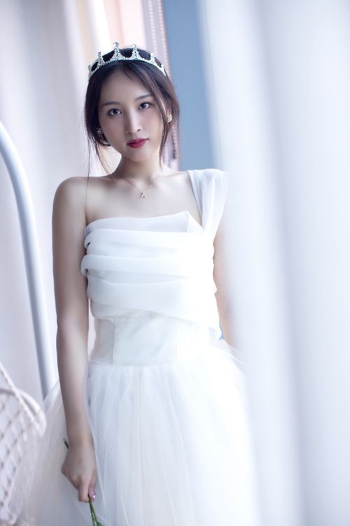 Free Graceful bride in a flowing white gown, adorned with a tiara, standing indoors with soft natural light. Stock Photo