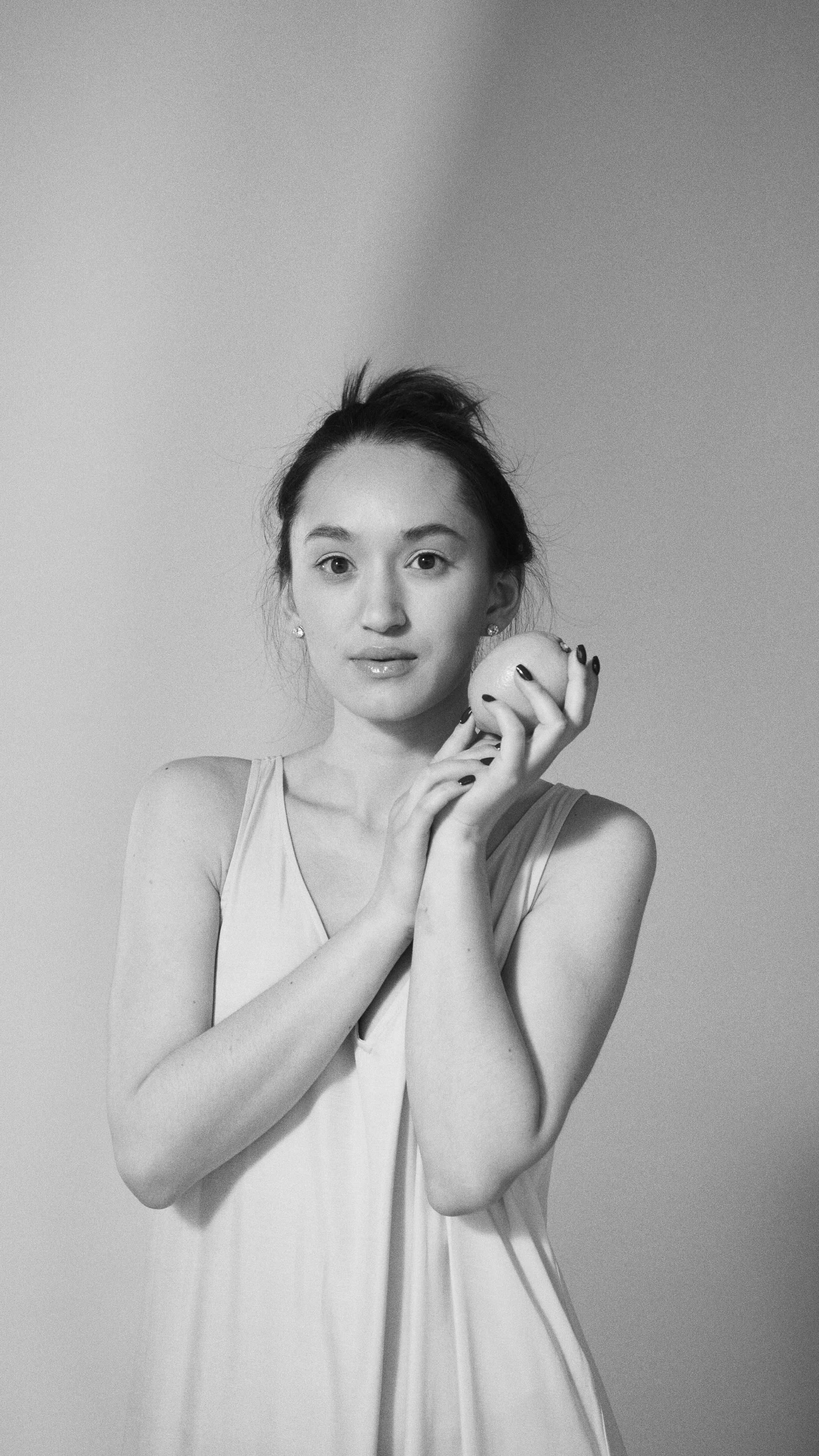 Monochrome portrait of a young adult woman holding a fruit, showcasing elegance and simplicity.