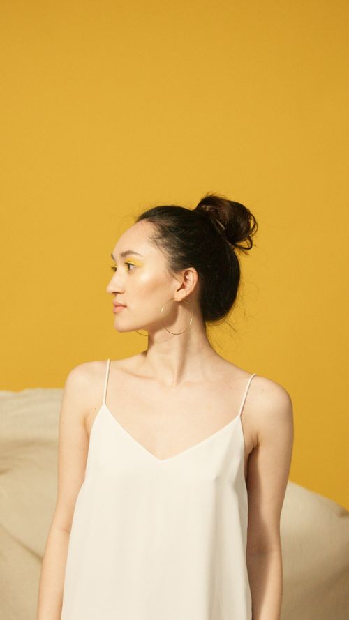 Free Studio portrait of a young woman with hoop earrings and a bun, looking sideways against a yellow backdrop. Stock Photo