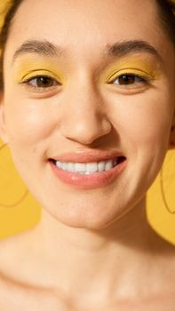 Close-up of a young woman with yellow eyeshadow and a cheerful smile.