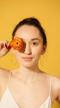 Portrait of a woman holding an orange flower against a vibrant yellow background.