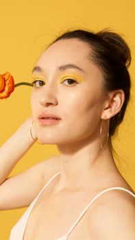 Portrait of a woman with yellow eyeshadow and hoop earrings posing gracefully with a floral accent.