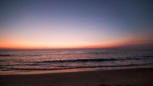 Free A peaceful beach scene at sunset, showcasing a calm ocean and colorful sky. Stock Photo