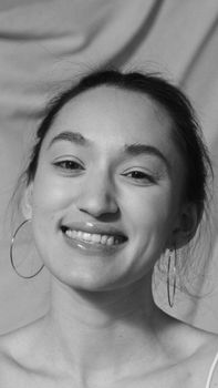 Close-up portrait of a smiling woman in black and white with hoop earrings.