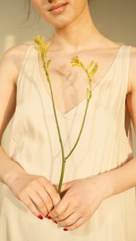 A woman in a beige dress holding a single yellow flower, exuding natural elegance.