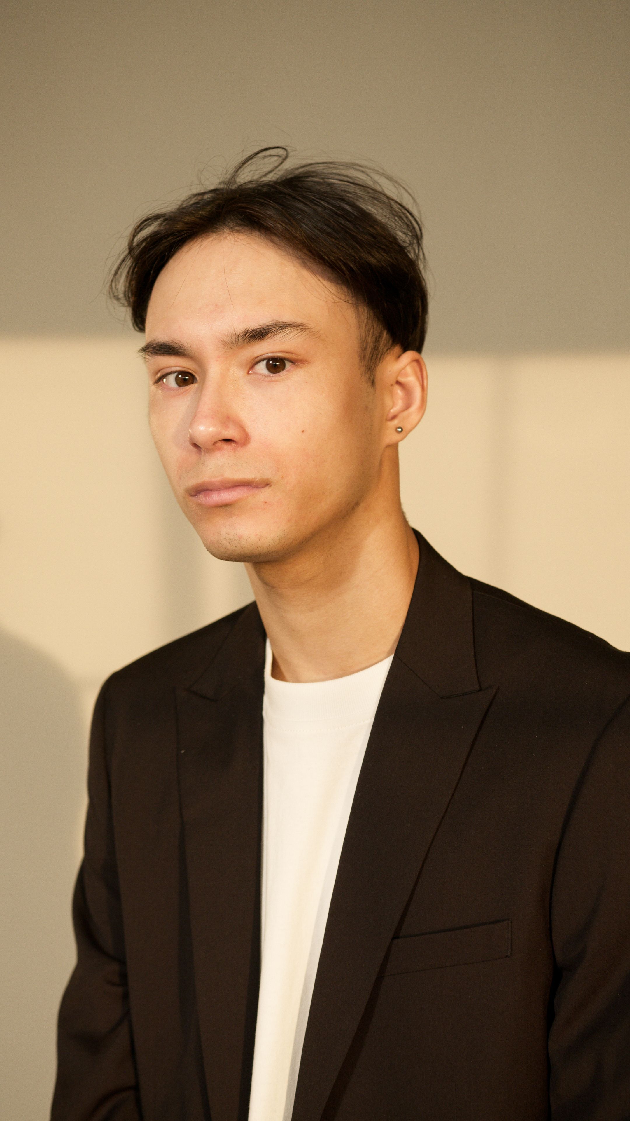 A professional portrait of a young man wearing a black suit indoors.