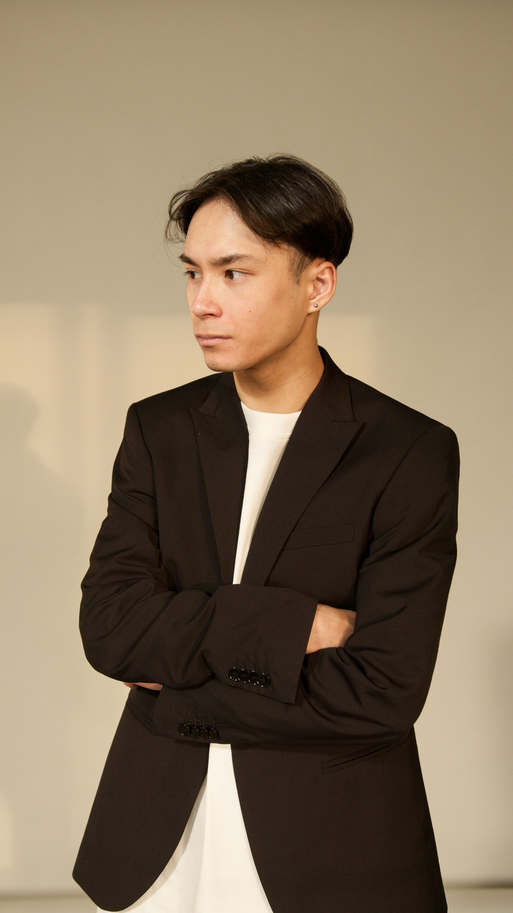 Portrait of a young East Asian man in a black blazer, looking thoughtful indoors.