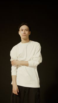 A man wearing a white sweater poses confidently against a dark backdrop, creating a striking contrast.