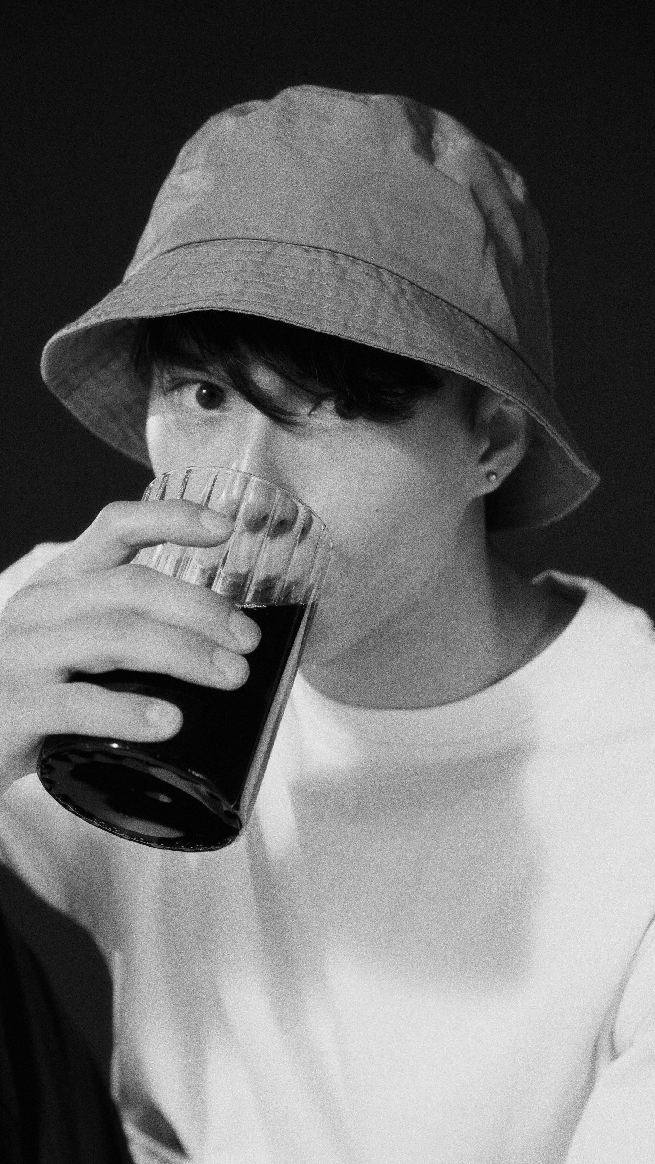 A grayscale portrait of a man wearing a bucket hat, drinking from a glass.