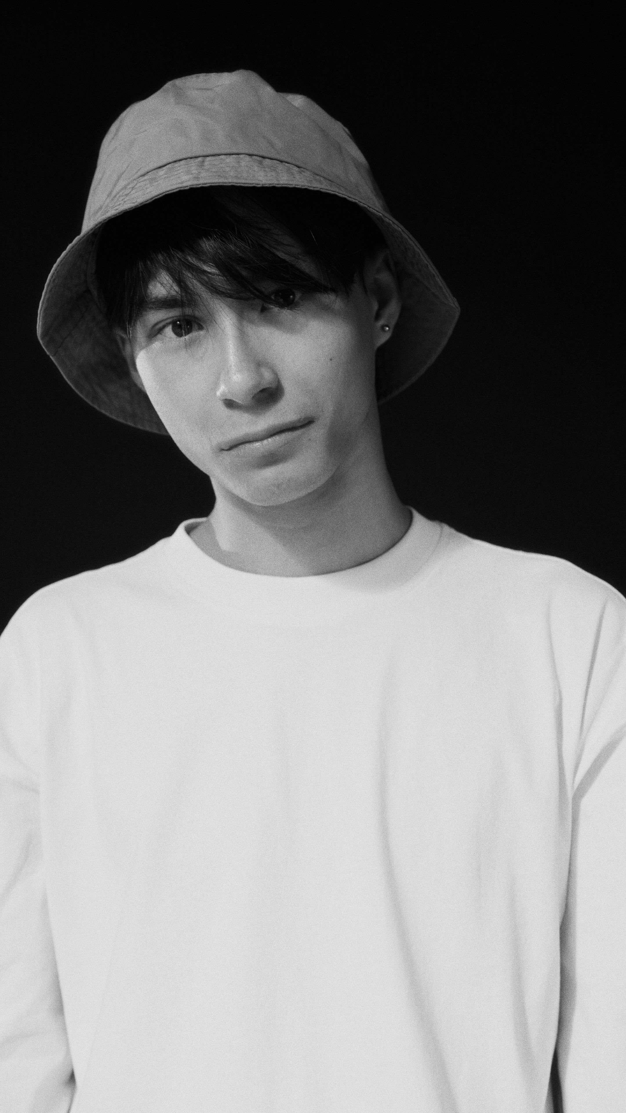 Black and white portrait of a young man wearing a hat and white shirt, with a neutral expression.