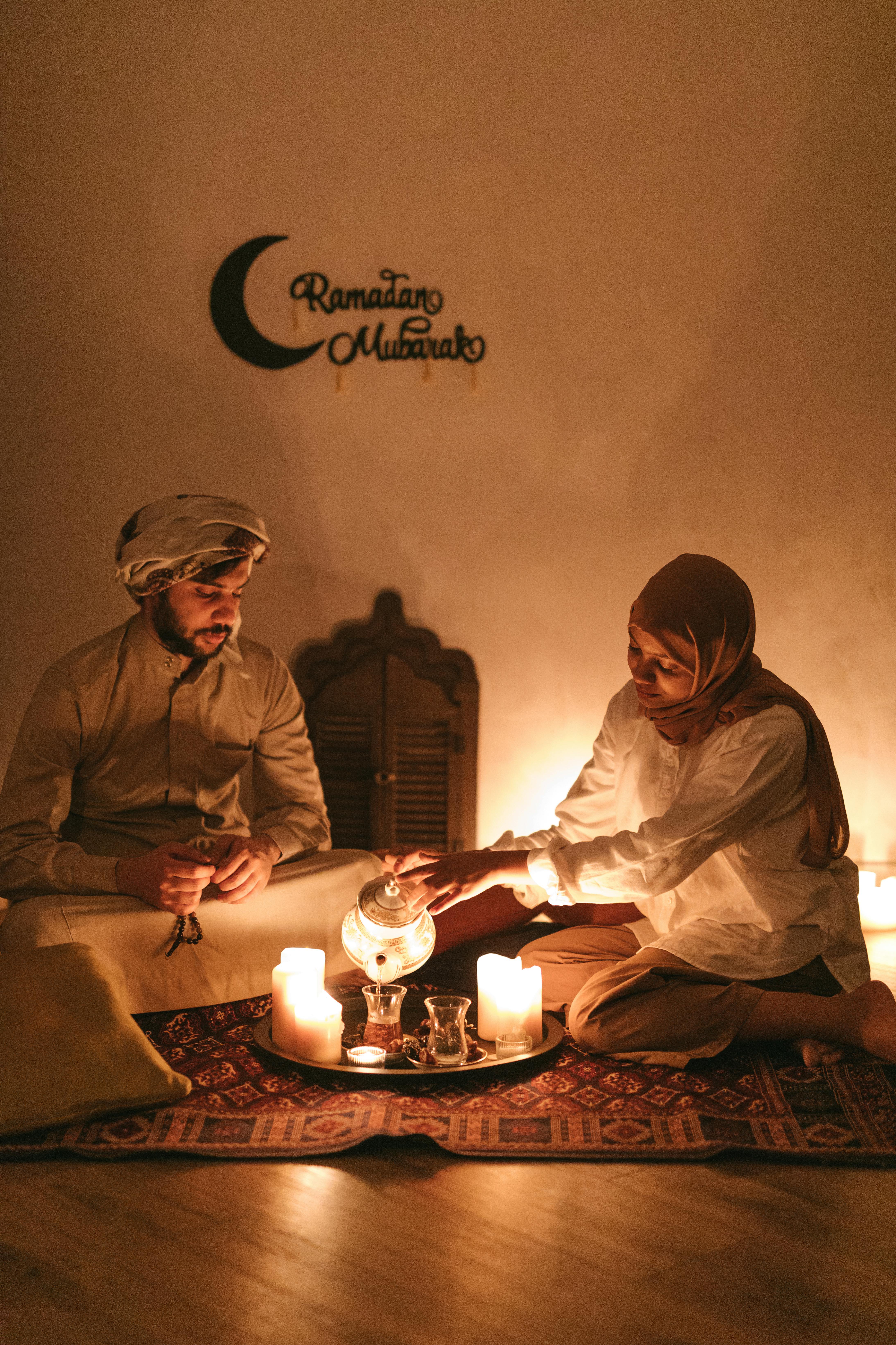 A couple enjoys a serene tea moment by candlelight, celebrating Ramadan indoors.