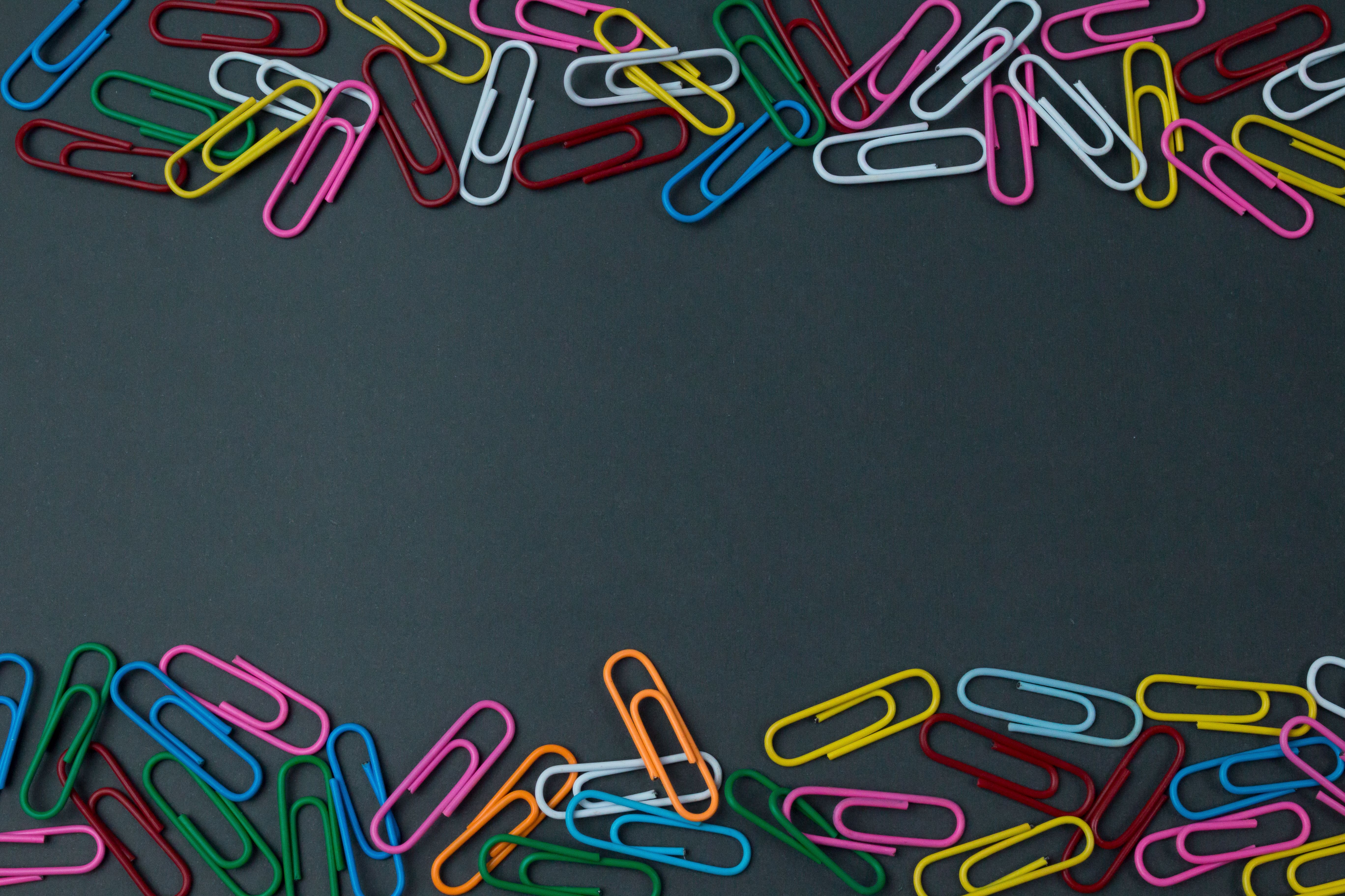 A variety of colorful paper clips arranged on a black surface with ample copy space.