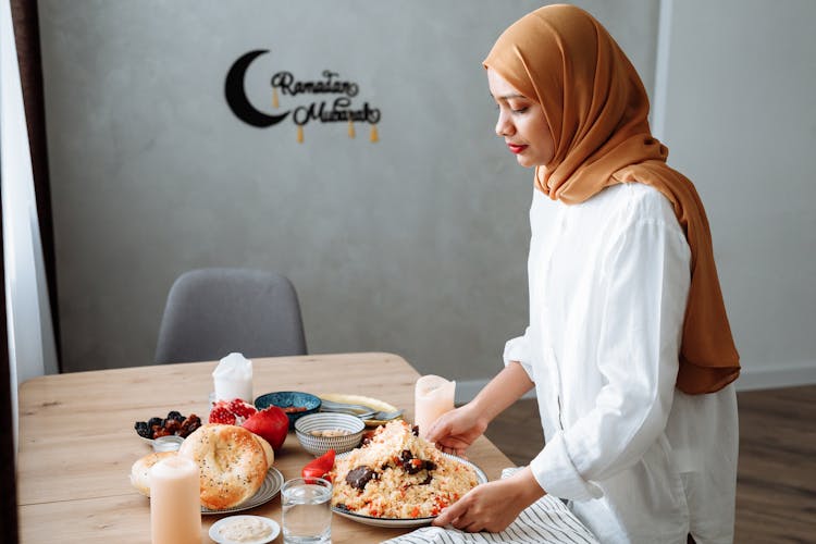 A Woman Wearing Hijab Serving The Food On The Table