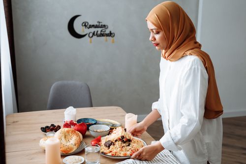 Free Muslim woman in hijab setting table with traditional iftar food during Ramadan. Stock Photo