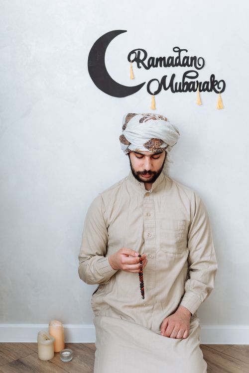 Free Man in traditional dress holding prayer beads during Ramadan prayer at home. Stock Photo