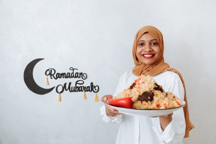 Woman In Brown Hijab Holding A Plate With Food