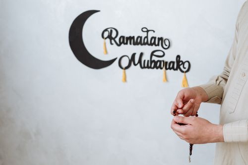 Free A Muslim man holding prayer beads with a Ramadan Mubarak wall decoration symbolizing the festive season. Stock Photo