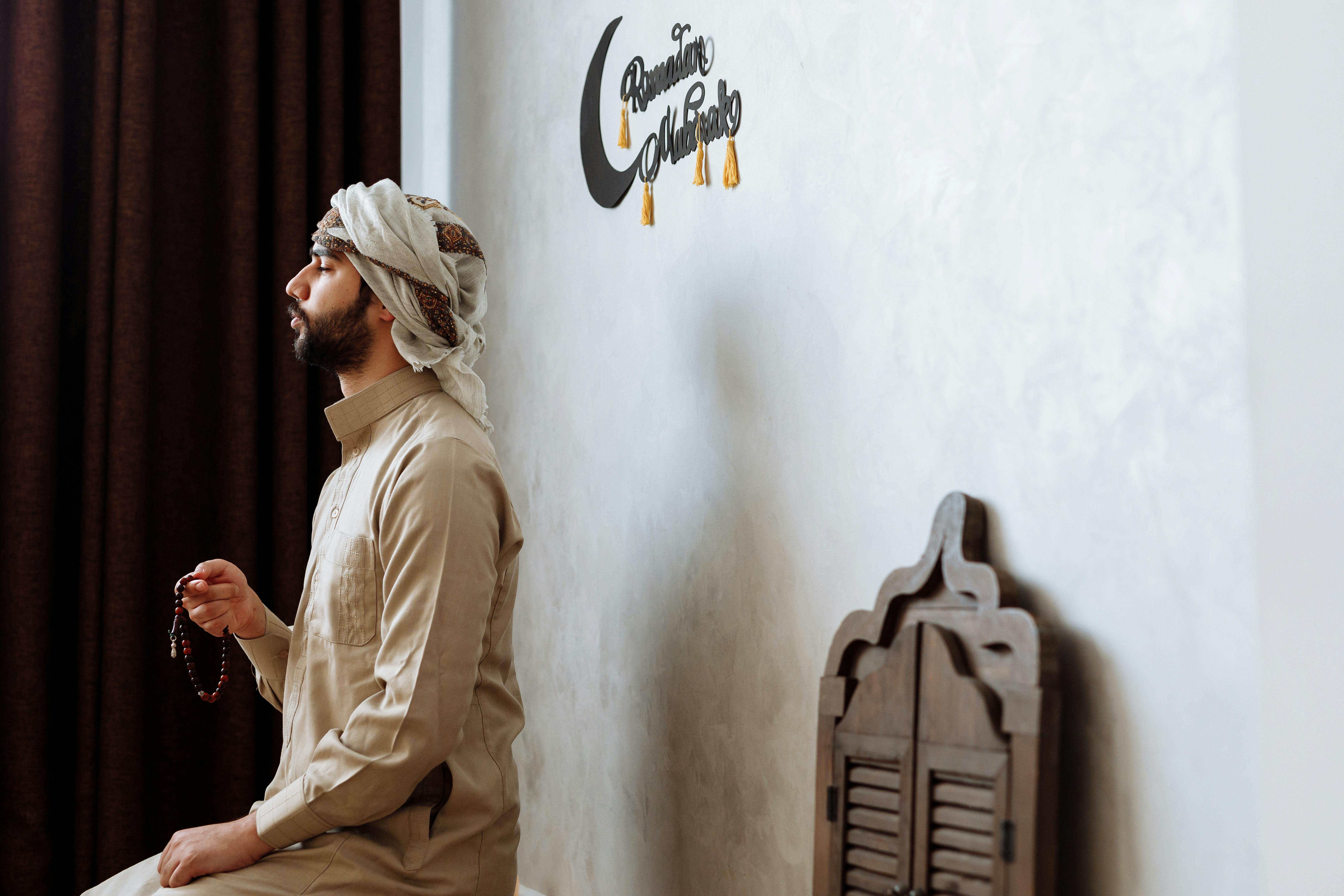 man in beige long sleeves traditional clothes sitting beside the concrete wall