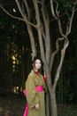 Woman in Green Long Sleeve Shirt Standing Beside Brown Tree