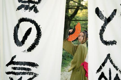 Woman in Green Kimono Standing Beside White and Black Banner With Japanese Calligraphy