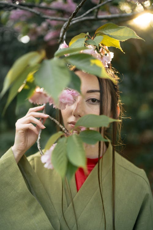 Free Woman in Green Kimono Looking At Pink Flowers Stock Photo