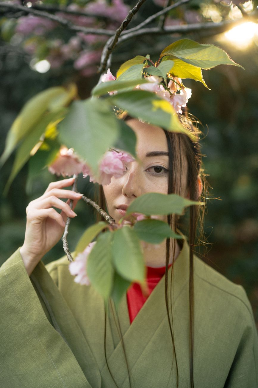 A contemplative portrait of a woman in a green kimono amidst cherry blossoms, blending nature and culture.