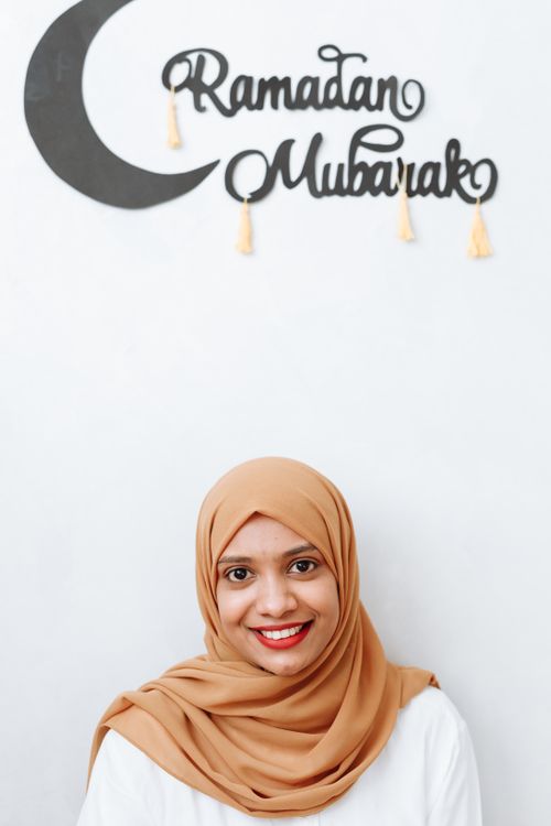 Free Woman in hijab smiling under a Ramadan Mubarak decoration at home. Stock Photo