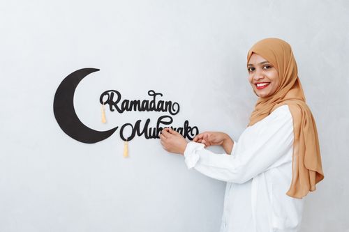 Free A woman in hijab hangs a decorative Ramadan Mubarak sign on the wall, expressing joy and festivity. Stock Photo