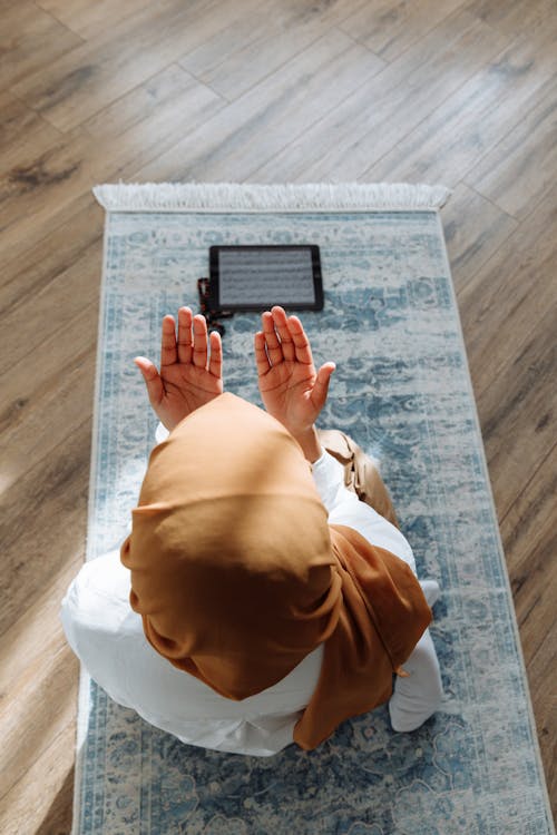 Free High-Angle Shot of a Person Kneeling on a Blue Prayer Rug Stock Photo