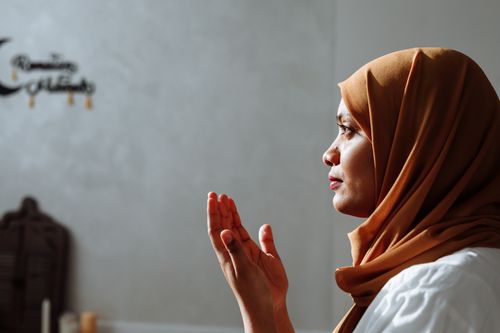 Free Side view of a Muslim woman in a brown hijab praying indoors with spiritual focus. Stock Photo