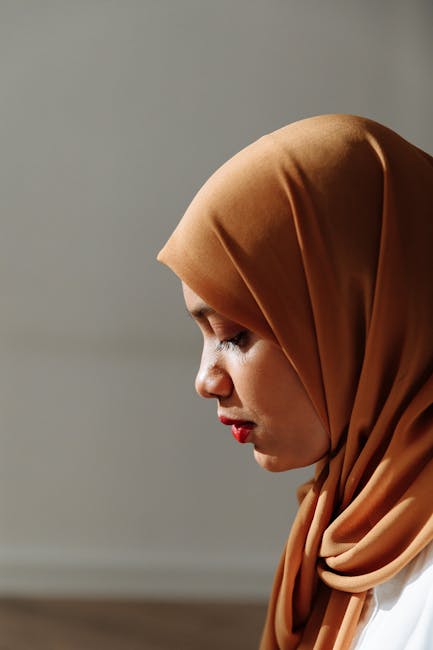 A serene side profile portrait of a woman wearing a traditional hijab, softly lit.