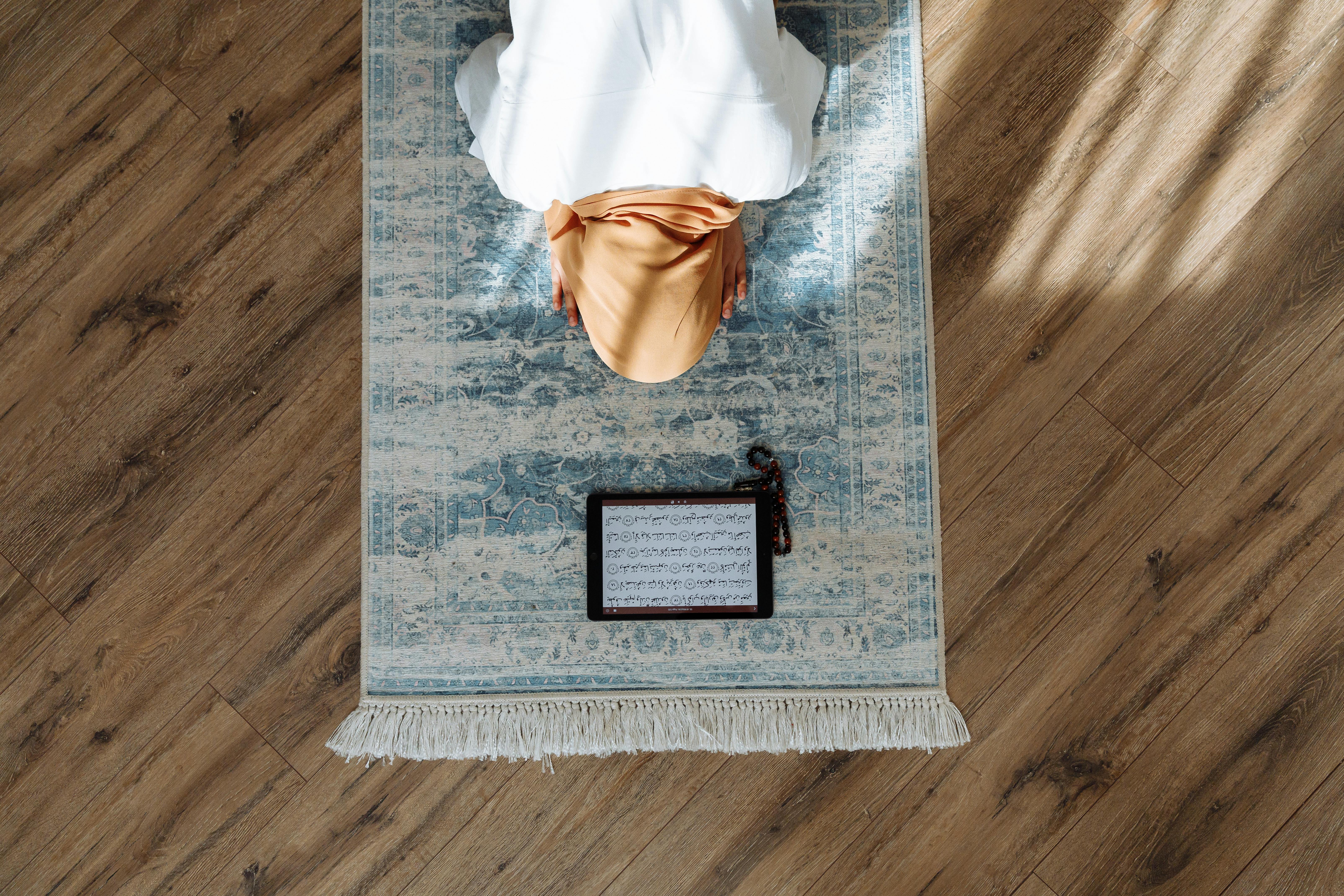 woman in brown hijab kneeling on prayer rug
