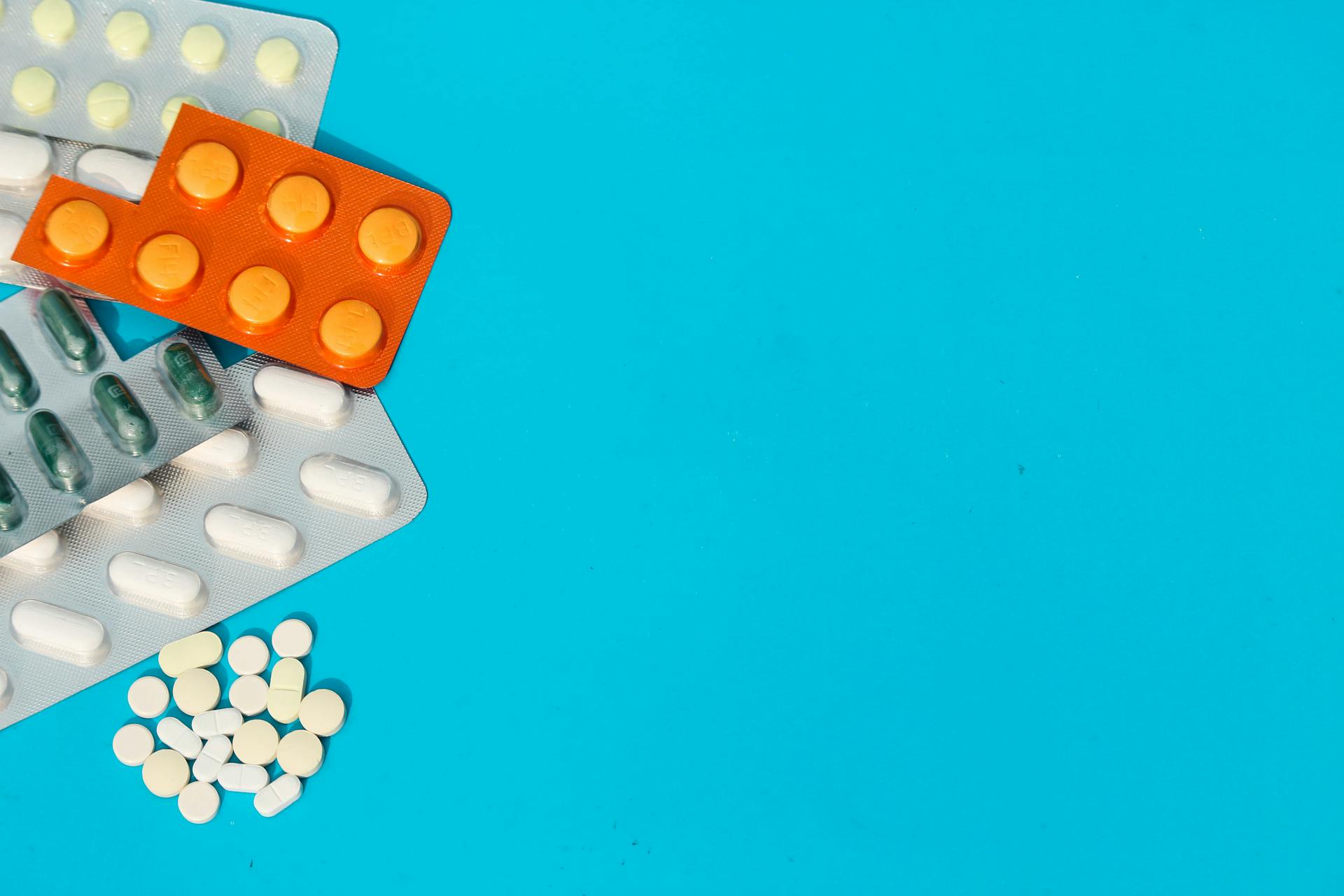 Colorful blister packs and loose pills on a blue backdrop with copy space.