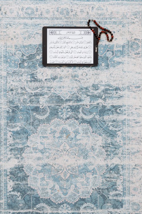 Tablet with Sacred Islamic Text and Praying Beads Lying on a Pale Blue Carpet