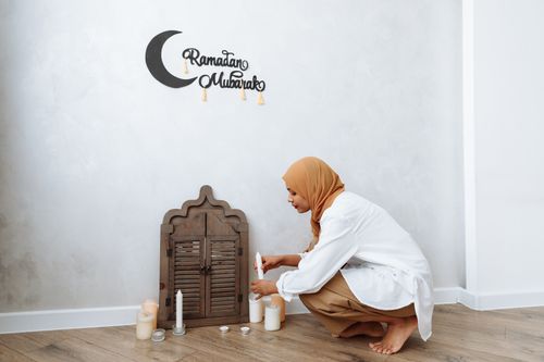 Free A woman in a hijab lights decorative candles for Ramadan indoors. Stock Photo
