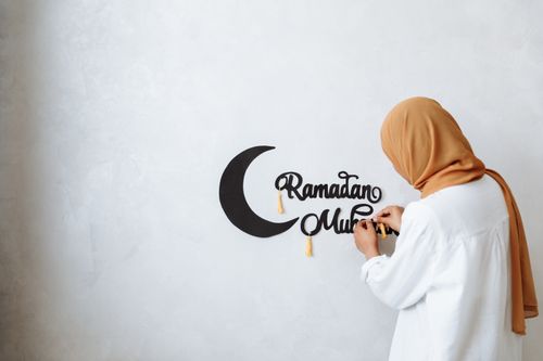 Free A woman in a hijab decorates a wall with Ramadan Mubarak inscriptions. Stock Photo
