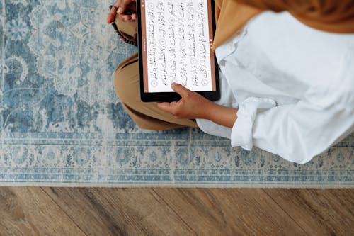 Free High Angle Shot of Woman in Brown Hijab reading Quran on a Tablet  Stock Photo