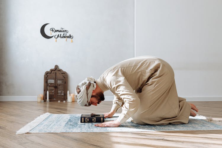 Man In Traditional Wear Kneeling On A Prayer Rug