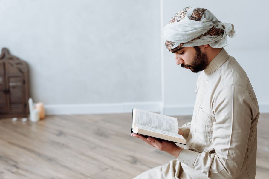 Seorang lelaki berpakaian tradisional Islam khusyuk membaca al-Quran di dalam