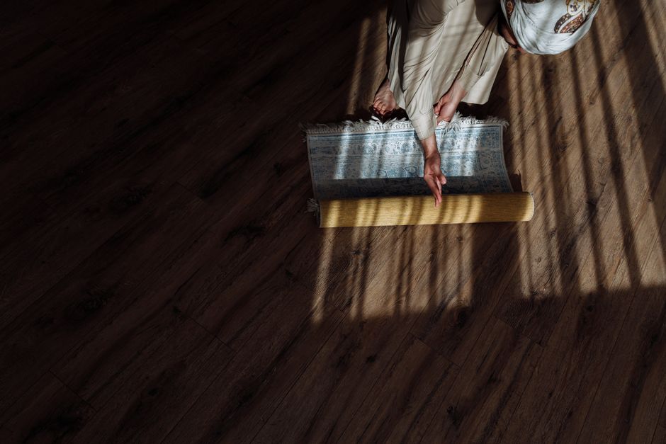 Aerial view of person preparing for prayer by rolling out a rug on a wooden floor.