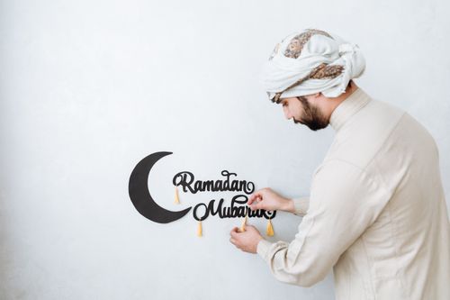 Free A man places a Ramadan Mubarak sign with decorative elements on a white wall. Stock Photo
