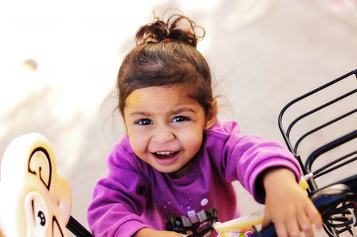 Free A joyful young girl enjoys a tricycle ride with a bright smile and playful energy. Stock Photo