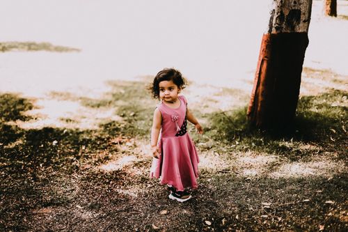 Free Adorable young girl in a pink dress enjoying an outdoor playtime. Warm daylight enhances her joyful expression. Stock Photo