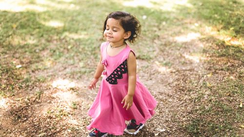 Free A joyful young girl in a pink dress enjoys a sunny day outdoors with eyes closed. Stock Photo