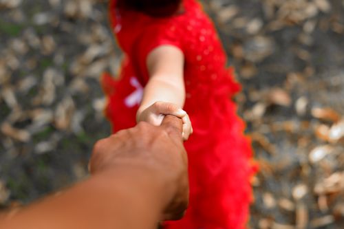 Free A child in a red dress holding an adult's hand outdoors, symbolizing love and connection. Stock Photo