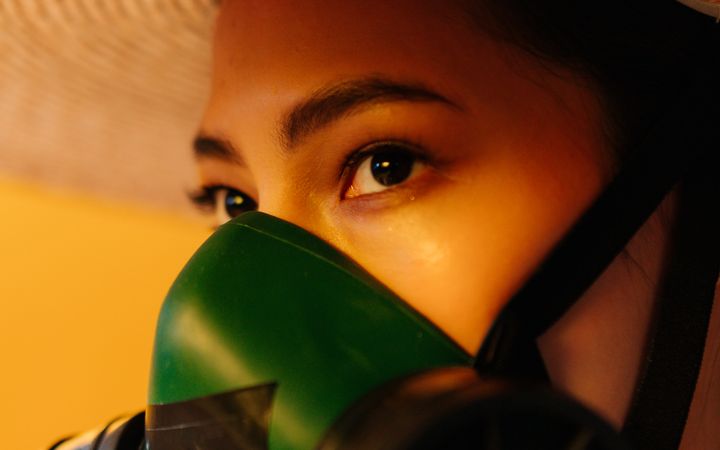 Close-up portrait of a woman in a straw hat with a respirator, conceptual studio shot.